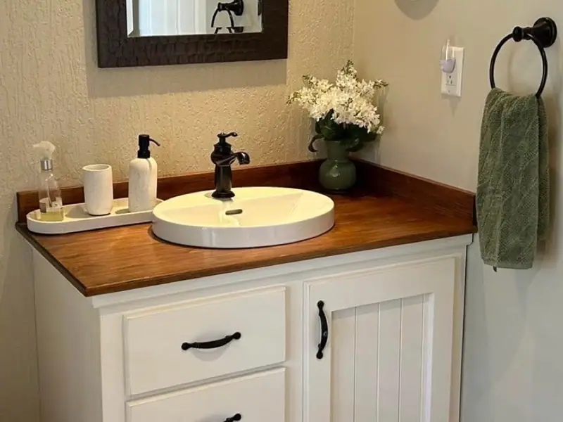 Vanité de salle de bain en pin peinte blanche, comptoir en planches de pin teint, lavabo ovale et robinet noir.