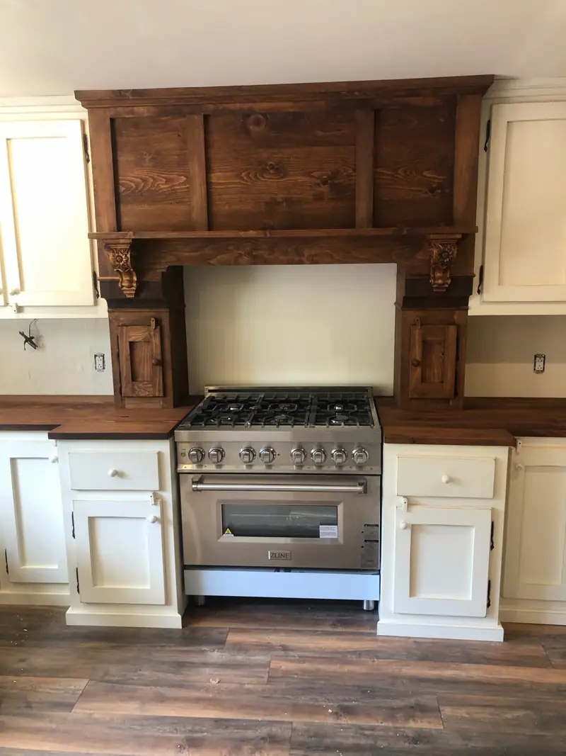 Hotte-manteau en pin massif teint noyer foncé à consoles sculptées, au-dessus d’une cuisinière au gaz.