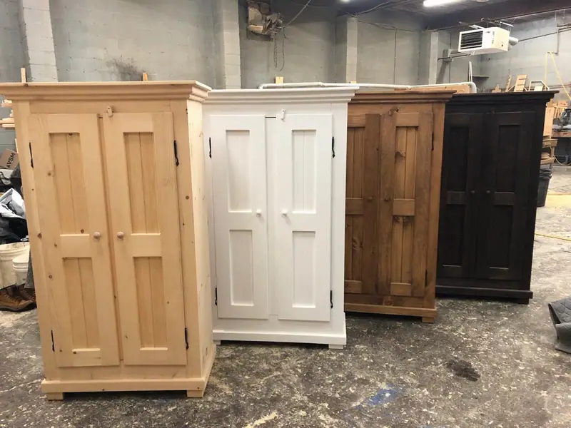 Quatre fois la même armoire Champêtre à portes de lambris alignées à l’atelier, dans quatre finitions : pin brut.