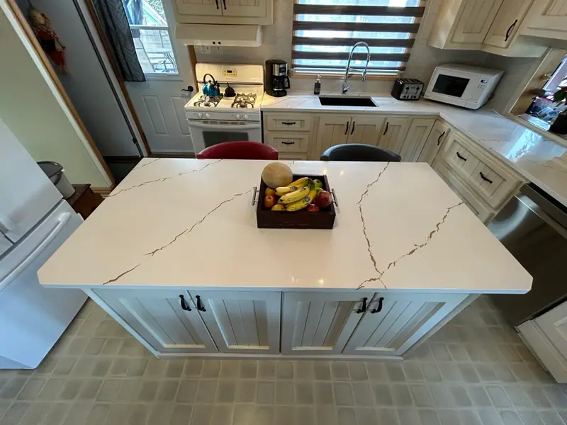 Îlot de cuisine en pin peint blanc cassé sous un comptoir de quartz, dans une cuisine blanche assortie