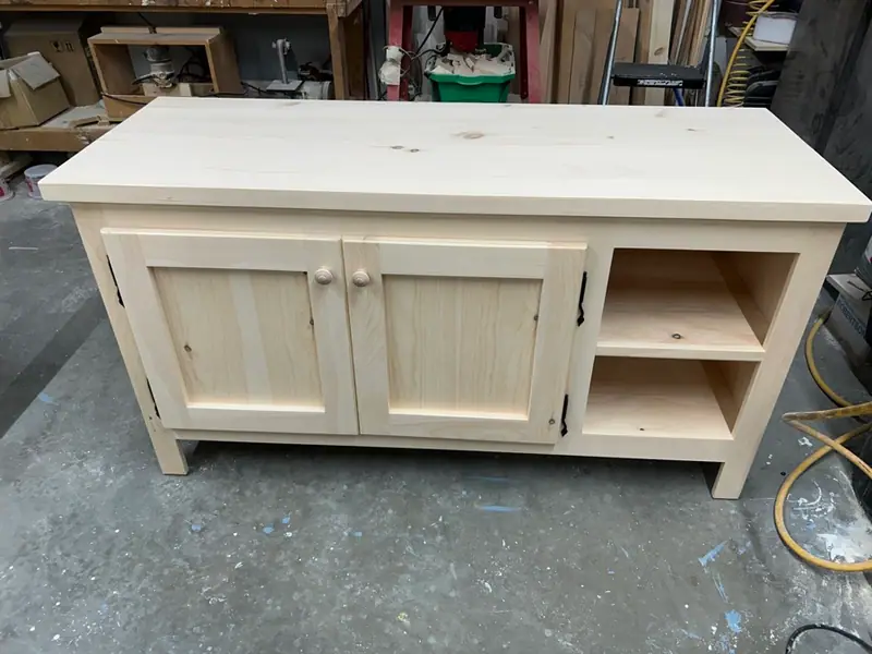Meuble à TV en pin naturel sans finition, deux portes et tablettes ouvertes, par un ébéniste près de La Conception.