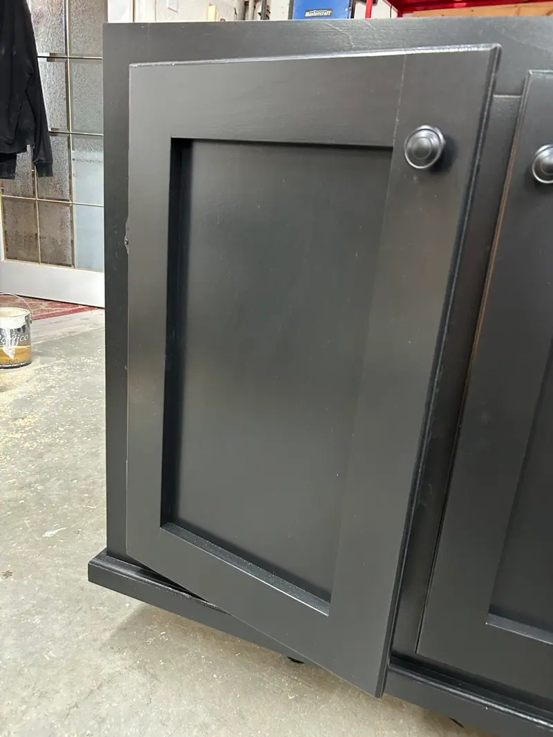 Porte à panneau shaker peinte en noir, entrouverte sur son caisson.
