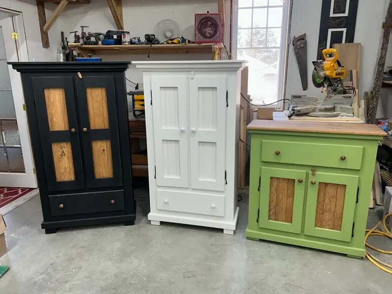 Trois meubles en pin à l’atelier : armoire noire à lambris, armoire blanche à moulure de couronnement et buffet vert lime.